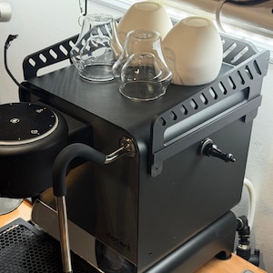 Könnte beinhalten: Eine schwarze Espressomaschine mit einer Dampflanze aus Edelstahl und einem schwarzen Griff. Zwei klare Gläser und zwei weiße Keramiktassen stehen obenauf. Das Wort "decent" ist auf der Vorderseite der Maschine zu sehen.