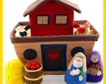 Könnte beinhalten: Ein Filz-Arche Noah Spielzeug-Set mit einem roten Haus, Tieren und Figuren. Die Arche ist beige mit einer blauen Tür und einem roten Herzen. Das Set enthält ein Fass mit roten Äpfeln, einen gelben Heuballen und zwei Figuren in Blau und Lila.