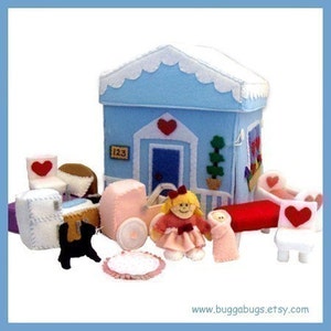 Puede incluir: Una casa de juegos de fieltro con un exterior azul, molduras blancas y un corazón rojo en la puerta. La casa está rodeada de muebles y juguetes de fieltro, incluyendo un cochecito, una cuna, una silla y una muñeca. La casa tiene el número "123" en el lateral.