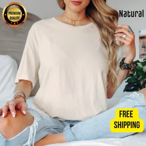K&ouml;nnte beinhalten: Cremefarbenes T-Shirt mit kurzen &Auml;rmeln. Das Shirt hat einen Rundhalsausschnitt und eine lockere Passform. Das Wort &bdquo;Natural&ldquo; ist in Schwarz rechts oben aufgedruckt. Ein goldfarbenes Abzeichen mit den Worten &bdquo;Premium Quality&ldquo; befindet sich oben links. Die Worte &bdquo;Free Shipping&ldquo; stehen in einer gelben Box.