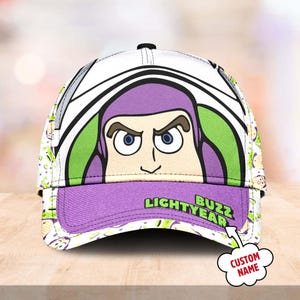 May include: A white and purple baseball cap with a cartoon image of Buzz Lightyear from the Toy Story franchise. The cap has a green and white pattern and the text "Buzz Lightyear" on the front.
