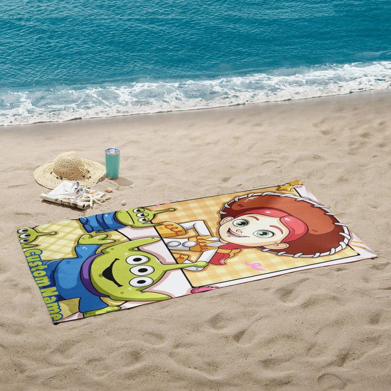 Puede incluir: Una toalla de playa rectangular con personajes de dibujos animados, incluyendo un extraterrestre verde de tres ojos y una vaquera. La toalla tiene un patr&oacute;n de cuadros amarillos y blancos y las palabras "Custom Name" est&aacute;n impresas en el lateral.