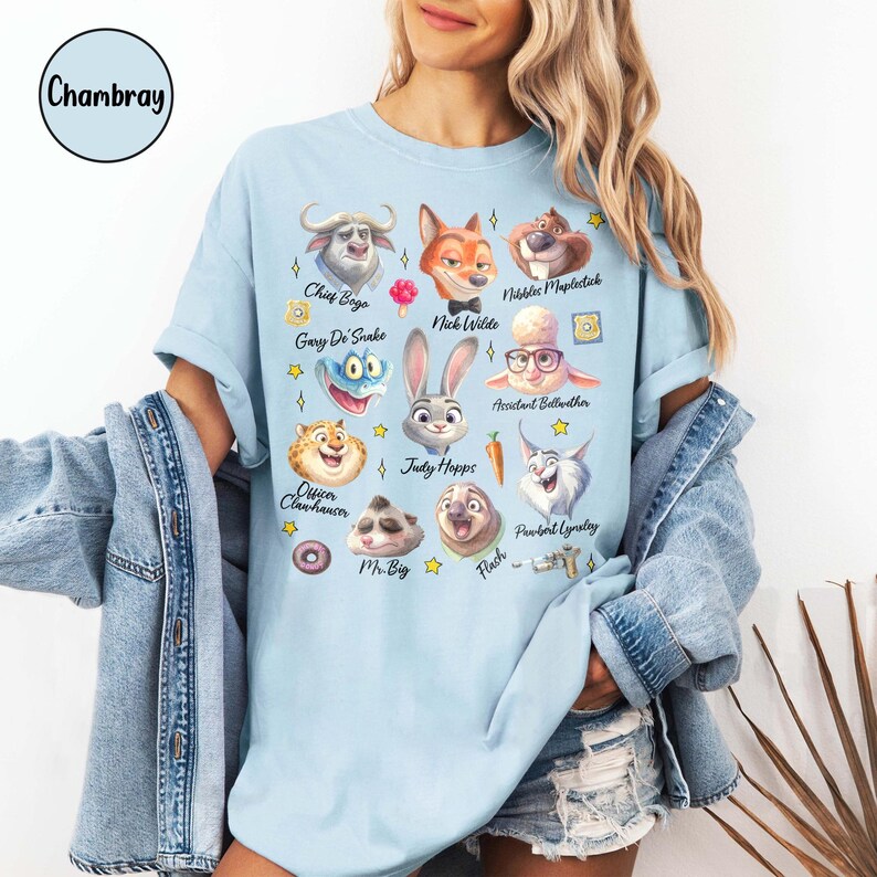 May include: Light blue t-shirt featuring cartoon illustrations of characters from Zootopia, including Chief Bogo, Nick Wilde, and Judy Hopps. The shirt has short sleeves and a crew neck. The word "Chambray" is in a circle in the upper left corner.