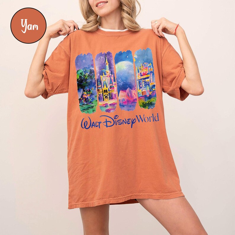 Puede incluir: Una camiseta naranja con cuatro im&aacute;genes coloridas de estilo acuarela de los monumentos de Disney World. Debajo de las im&aacute;genes est&aacute; el texto "Walt Disney World" en azul. La camiseta tiene mangas cortas y un corte holgado.