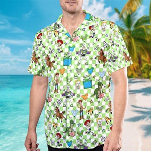 May include: A short-sleeved button-down shirt featuring a green and white checkered pattern. The shirt is adorned with various cartoon characters and stars. The collar and inner cuffs have a contrasting blue trim. The shirt is made of a lightweight fabric.