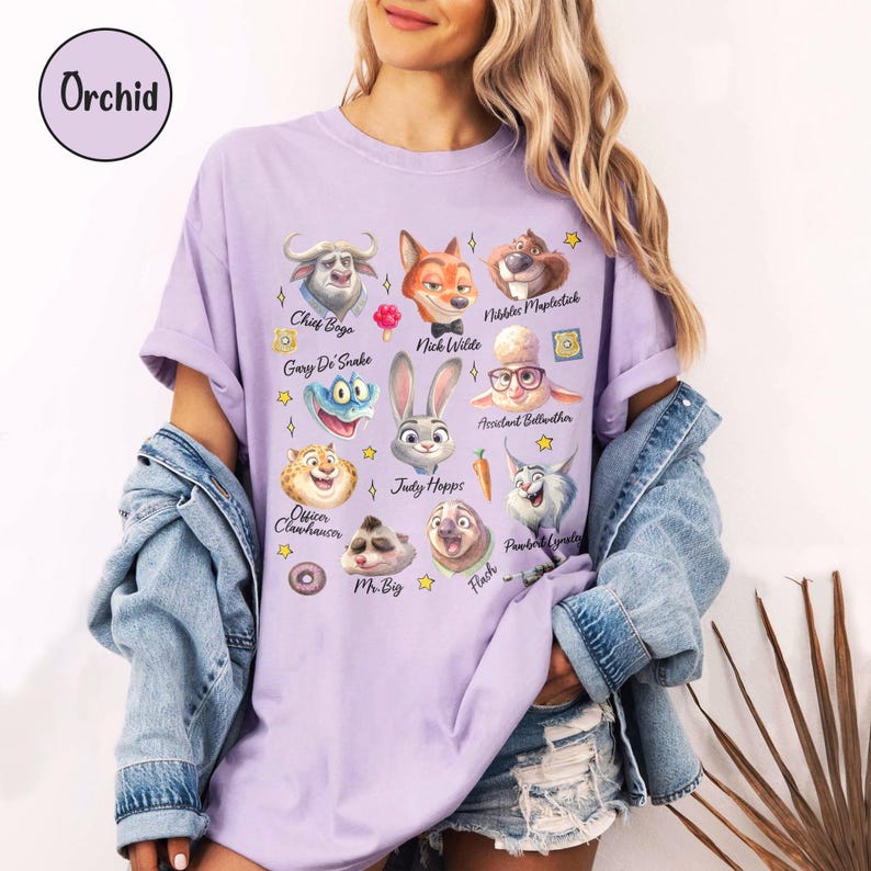 May include: A light purple t-shirt featuring cartoon character illustrations from a movie. The shirt includes the text "Orchid" at the top left. The illustrations include characters such as Judy Hopps, Nick Wilde, and Chief Bogo.