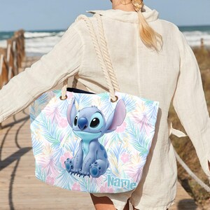 May include: A large tote bag with a blue cartoon character design, set against a backdrop of pastel tropical leaves and flowers. The bag has rope handles and the word "Name" is printed on the bottom right.