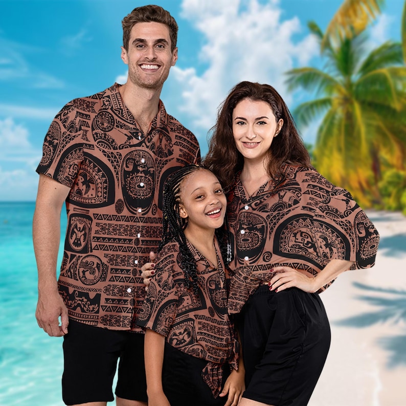 May include: A family of three wearing matching brown and black patterned shirts with a Polynesian design. The shirts have short sleeves and a button-up front. The family is standing in front of a beach scene.