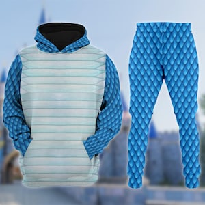 May include: A blue two-piece outfit comprising a hoodie and leggings. The hoodie has a light blue and white striped front with blue scale-patterned sleeves. The leggings are covered in a blue scale pattern. The outfit is set against a blurred background.