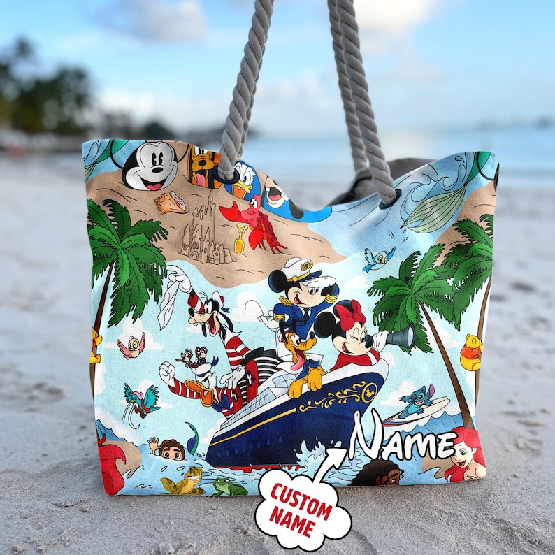 May include: A blue and white beach tote bag with a colorful Disney character print. The bag features Mickey Mouse, Minnie Mouse, Donald Duck, Goofy, and other Disney characters. The bag has a large pocket on the front and a handle on the top. The bag has the text "Name" and "Custom Name" on it.