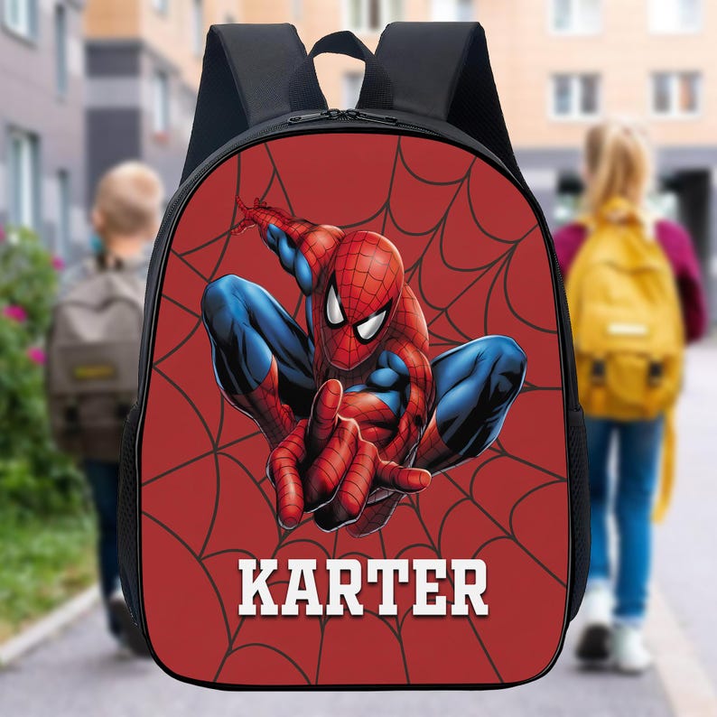 May include: A black backpack featuring a red front panel with a graphic of the character Spider-Man in a crouching pose over a black spiderweb pattern. The name KARTER is printed in white block letters at the bottom of the red panel.