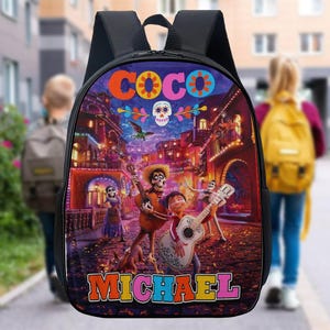 May include: Black backpack with a colourful illustration from the film "Coco." The design features characters playing guitars in a vibrant street scene, with the name "MICHAEL" in bold letters at the bottom.