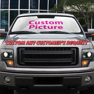 May include: A grey pickup truck with a custom picture sunshade. The sunshade is white with the words "Custom Picture" in pink letters. The truck has a black grille and headlights. The text "CUSTOM ANY CUSTOMER'S REQUEST" is printed in red letters on the front of the truck.