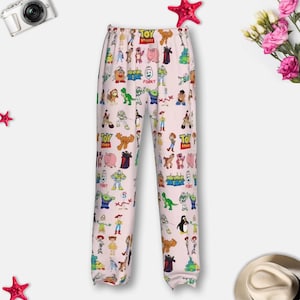 May include: Pale pink pajama trousers with a vibrant pattern of Toy Story characters. The trousers have an elasticated waistband and a loose fit. The design includes characters such as Woody, Buzz Lightyear, and other characters from the animated film.
