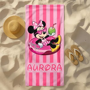 May include: A rectangular beach towel with vertical pink and light pink stripes. The center features Minnie Mouse wearing heart-shaped sunglasses and a polka dot outfit, floating in a pink inner tube while holding a green coconut drink. The name AURORA is printed in large pink letters at the bottom.