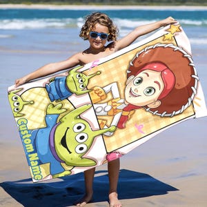 Puede incluir: Una toalla de playa rectangular con personajes de dibujos animados de Toy Story. La toalla tiene un fondo claro con un patr&oacute;n repetitivo. Los personajes incluyen a los Little Green Men y a Jessie la vaquera. Las palabras "Custom Name" est&aacute;n impresas en la toalla.