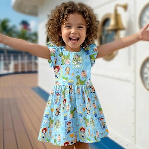 Puede incluir: Un vestido azul claro con un estampado de personajes de la pel&iacute;cula Toy Story. El vestido tiene mangas cortas con volantes y una falda fruncida. La ni&ntilde;a de la imagen sonr&iacute;e con los brazos extendidos.