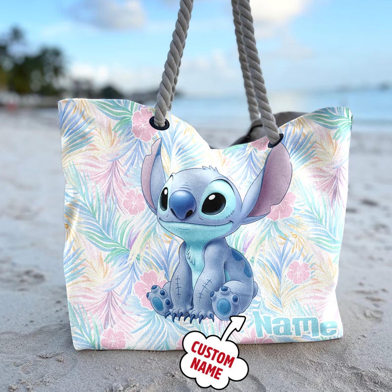 May include: A beach tote bag with a cartoon character design, set against a tropical floral pattern in pastel shades. The bag has grey rope handles. The word "Name" is printed on the bag.