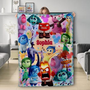May include: A colourful fleece blanket featuring characters from the film Inside Out. The blanket has a pink, blue and yellow background with images of Joy, Sadness, Anger, Disgust and Fear. The blanket is personalised with the name "Sophia".