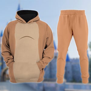 May include: A brown hoodie and matching pants set. The hoodie features a black-lined hood and a light brown panel on the front with a curved design. The pants are a solid light brown color, with a drawstring waist and fitted ankles.
