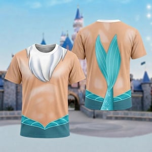 May include: A short-sleeved t-shirt featuring a tan skin-toned base with a white beard graphic on the front neckline. The back displays a large teal mermaid tail graphic extending from the hem, with teal accents along the bottom edge.
