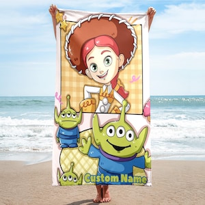 Puede incluir: Toalla de playa con una ilustraci&oacute;n de dibujos animados de Jessie de Toy Story, con sombrero de vaquero marr&oacute;n y pelo rojo. La toalla tambi&eacute;n incluye extraterrestres verdes y el texto "Custom Name".