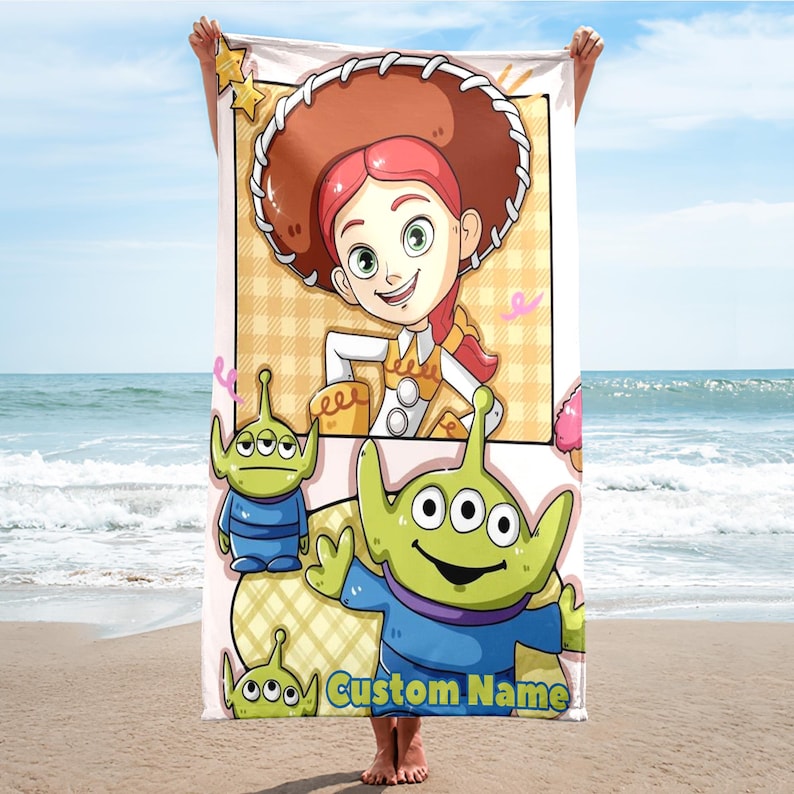 Puede incluir: Toalla de playa con una ilustraci&oacute;n de dibujos animados de Jessie de Toy Story, con sombrero de vaquero marr&oacute;n y pelo rojo. La toalla tambi&eacute;n incluye extraterrestres verdes y el texto "Custom Name".