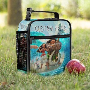 May include: A blue lunch bag featuring characters from the animated movie Moana. The bag has a black handle, a side mesh pocket, and a front zipper. The words "CUSTOM NAME" are printed on the top of the bag.