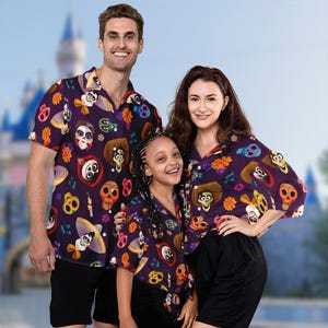 May include: A family of three wearing matching purple, black, and yellow short-sleeved shirts with a colorful print of characters from the movie Coco. The shirts feature images of Miguel, Hector, and Dante.