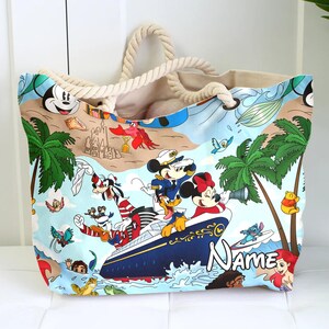 May include: A large canvas tote bag with a nautical theme featuring Mickey Mouse, Minnie Mouse, Goofy, Donald Duck, and Stitch. The bag has a rope handle and a blue and white design with the text "Name" on the bottom.