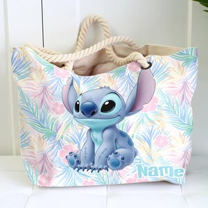 May include: A large tote bag with a tropical floral pattern in pastel colours. The bag features a cartoon image of Stitch, with the word "Name" printed in a light blue font. The bag has rope handles.