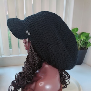 Peut inclure: Un bonnet noir en crochet avec une visière et un bandeau en crochet marron. Le bonnet est sur une tête de mannequin blanche.