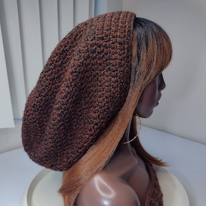 May include: A brown and black crocheted beanie with a slouchy fit. The beanie is worn on a mannequin with long, brown hair.