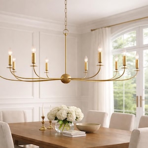 以下が含まれることがあります： 木製のダイニングテーブルの上に、10個のろうそく型のライトが付いたゴールドトーンのシャンデリアが吊り下げられています。 部屋には白い壁、大きな窓、白い花の入った花瓶があります。 シャンデリアのアームは水平に伸びており、バランスの取れたエレガントなデザインになっています。