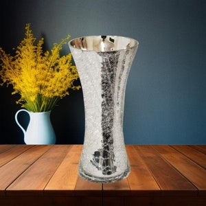May include: A silver crackle glass vase with a wide mouth and a narrow base. The vase is sitting on a wooden table.