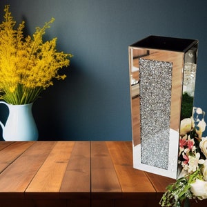 May include: A tall, silver mirrored vase with a diamond-like pattern. The vase is empty and has a square shape.