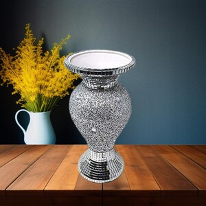 May include: A silver mirrored mosaic vase with a textured surface. The vase has a wide base and a narrow neck.