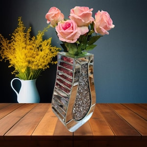 May include: A mirrored vase with a diamond-like texture and pink and red stripes. The vase is filled with pink silk roses.