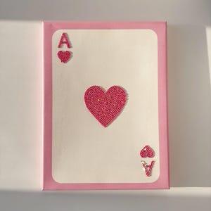 Peut inclure: Une peinture sur toile rose repr&eacute;sentant l'As de Coeur. La carte est faite de strass roses et a une bordure rose.