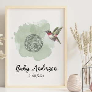 Può includere: Una stampa incorniciata con uno sfondo ad acquerello in tonalità di verde. Un colibrì con la testa rossa e le ali nere vola vicino a una sfera di vetro trasparente. Il testo "Baby Anderson 01/01/2024" è stampato sotto l'immagine.