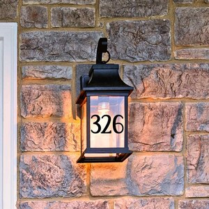May include: A black metal lantern with a glass front, mounted on a brick wall. The lantern has a light inside and the number 326 is visible on the glass.