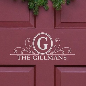 May include: A white vinyl decal with a decorative flourish and the letter "G" in a circle. The text "THE GILLMANS" is below the letter.
