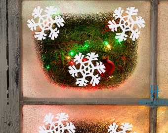 May include: A window with a frosted glass pane decorated with white paper snowflakes. A green garland with red and white lights is draped over the window. The text "HOUSEHOLDWORDS" is visible in the bottom right corner of the image.
