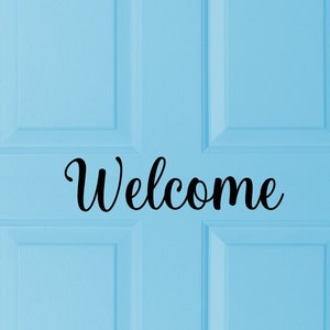 May include: A light blue door with the word "Welcome" in elegant black script. The door has a paneled design, and the text is centered, creating a welcoming aesthetic. The image is a close-up of the door.
