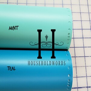 Puede incluir: Dos rollos de pel&iacute;cula adhesiva de vinilo, uno azul verdoso y otro verde menta, con el texto "HOUSEHOLDWORDS" impreso en el rollo azul verdoso.