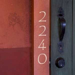May include: A close-up of a wooden door with a black door handle and a white number "2240" painted on the side. The door is painted a dark green color.
