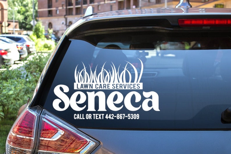 May include: White vinyl decal on a car window. The decal reads "Lawn Care Services Seneca" with a grass design above the text. The phone number 442-867-5309 is also included. The decal is on a dark grey car.