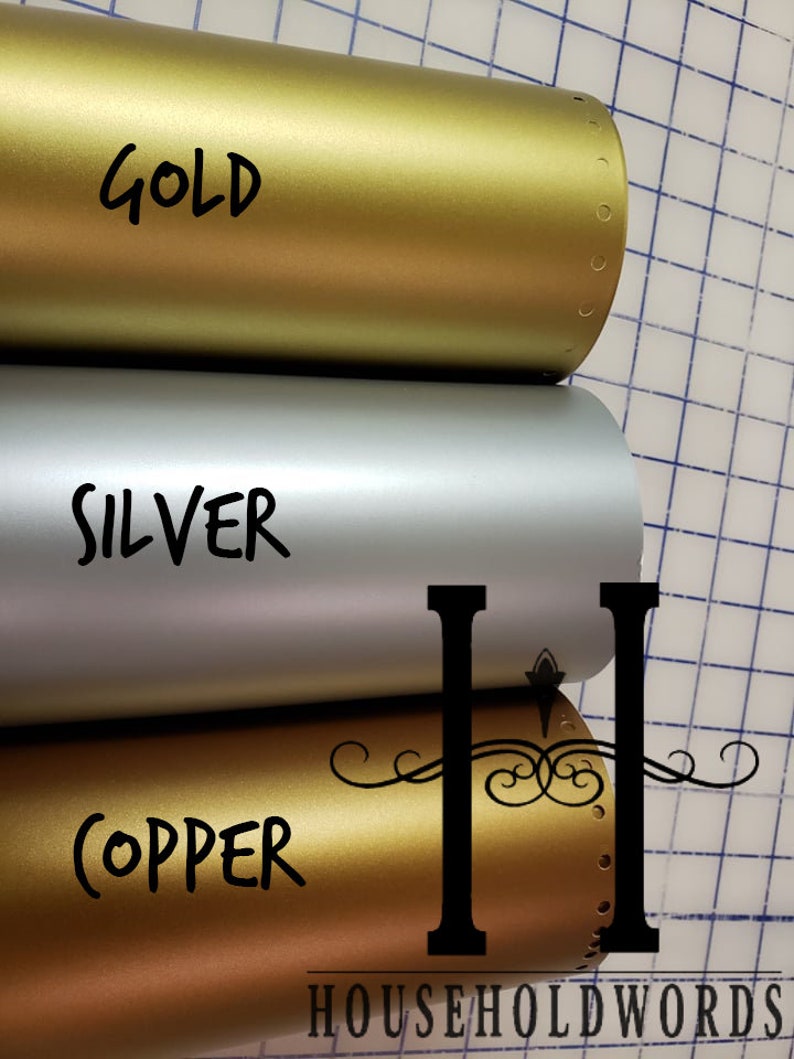 Puede incluir: Tres rollos de vinilo met&aacute;lico en oro, plata y cobre. Los rollos est&aacute;n etiquetados con los nombres de los colores. Los rollos est&aacute;n sobre un fondo de cuadr&iacute;cula.