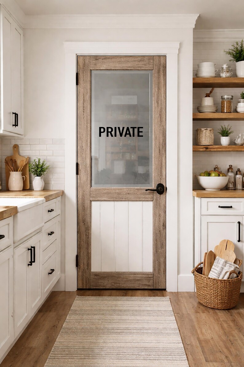 May include: A rustic wooden door with a glass panel etched with the word "PRIVATE" in black. The door is framed by light-colored wood and features a black handle. The lower portion of the door is white, with vertical paneling. The door is in a kitchen setting.