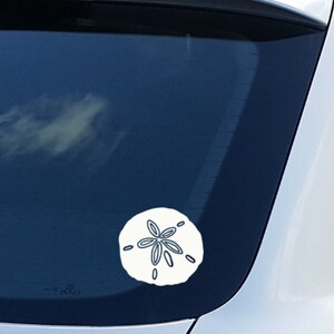 May include: A white car with a white sand dollar sticker on the back window.